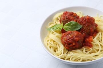 Delicious pasta with meatballs in bowl on white tiled table, closeup. Space for text