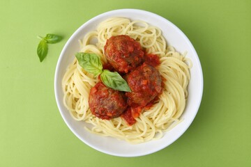 Delicious pasta with meatballs in bowl on green table, top view