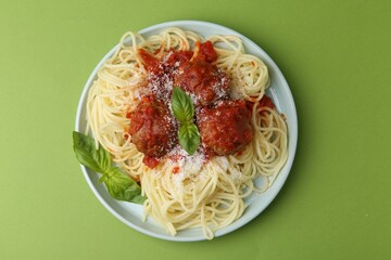 Delicious pasta with meatballs, basil and cheese on green table, top view
