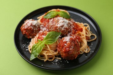 Delicious pasta with meatballs, basil and cheese on green table, closeup