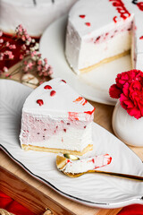 piece of raspberry cheesecake with buttercream on a white ceramic plate, red cake decoration, low-calorie cheesecake with berries, red background, red flowers, gypsophila, golden dessert spoon