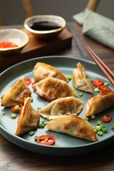 Delicious fried gyoza dumplings with green onions and chili peppers served on wooden table, closeup