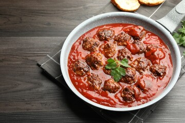Delicious meatballs with tomato sauce in frying pan on wooden table, closeup. Space for text