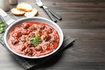 Delicious meatballs with tomato sauce in frying pan on wooden table, closeup. Space for text