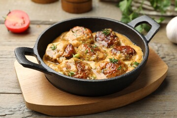 Delicious meatballs with gravy cream sauce and herbs on wooden table, closeup