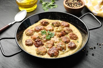 Delicious meatballs with gravy cream sauce and herbs served on black table, closeup