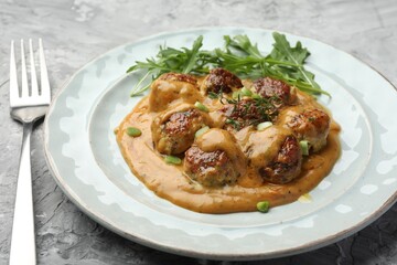 Delicious meatballs with gravy cream sauce, herbs and arugula served on grey table, closeup