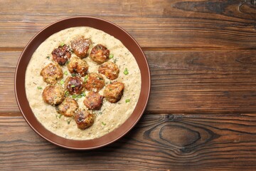 Delicious meatballs with gravy cream sauce and herbs on wooden table, top view. Space for text