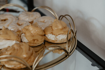 A beautifully arranged selection of caramel-glazed cream puffs with a crispy pastry shell, filled with fluffy whipped cream, elegantly displayed on a golden tray with a reflective surface at a bakery 