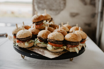 A delicious platter of gourmet mini burgers with sesame seed buns, fresh lettuce, juicy tomatoes, and perfectly grilled beef patties, each secured with a wooden skewer