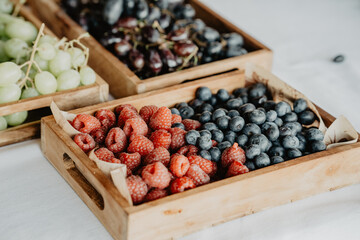 A beautifully arranged selection of fresh berries and grapes displayed in rustic wooden crates, featuring vibrant red raspberries, plump blueberries, green grapes, and dark purple grapes 