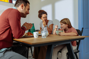 Parents watching their daughter eat breakfast