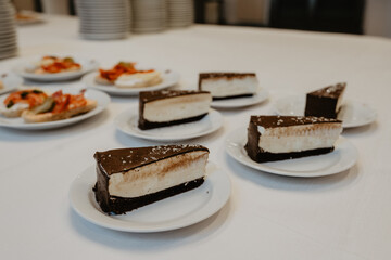 A beautifully arranged dessert table featuring multiple slices of rich chocolate-covered cheesecake with a creamy filling and dark cocoa crust, elegantly served on white plates