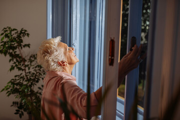 Happy elderly woman inhales fresh air on the window