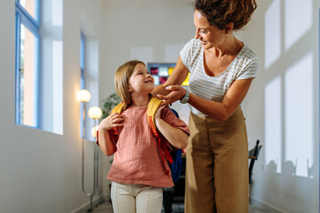 Mother helping her daughter put on a backpack
