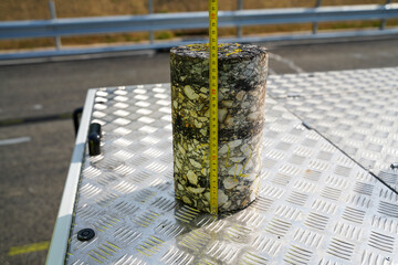 Worker Inspecting Cylindrical Core Sample Cut from Asphalt Road to Evaluate Paving Quality