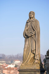 Obraz premium The image features a statue of a woman in a cloak with a pensive expression, standing against a clear blue sky