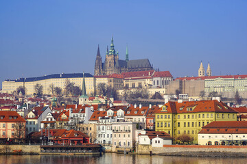 Fototapeta premium A breathtaking view of a historic European city showcases colorful buildings with red rooftops along the river, with a majestic castle and cathedral towering in the background