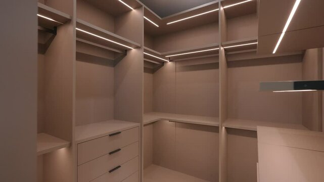Modern well organized walk in closet with ample storage space. Closet features multiple shelves, drawers and hanging rods, all illuminated by built in lighting