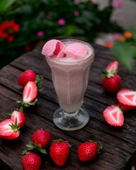 Strawberry milkshake with strawberry garnish served on a wooden table with a garden background