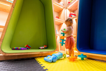 Child exploring a modern playroom with soft flooring, creative shelves, and fun activity toys