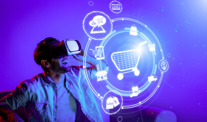Happy man using VR headset and shopping online while sitting at sofa with shopping bags. Smart person looking at online market hologram and icon with neon background. Innovation technology. Deviation.