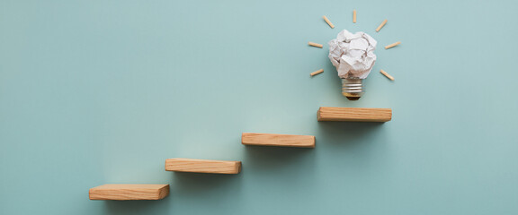 A creative business growth representation with wooden blocks forming a staircase and a crumpled paper lightbulb, symbolizing new ideas, innovation, and upward progress in business.