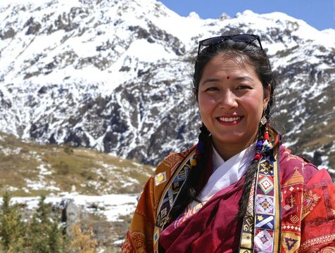 Radiant Tibetan Woman in Traditional Chuba Against Majestic Snowy Peaks