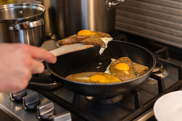 Man turns fried eggs with bread with wooden spatula. 