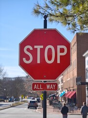 Obraz premium Bright red stop sign stands against a clear blue sky in a busy urban setting with pedestrians and shops nearby