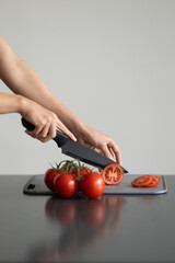 Red cocktail tomatoes on cutting board. Girl slicing tomatoes with knife for salad. Home cooking and food concept. Fresh organic vegetables, healthy food, ingredient. Cherry tomatoes on branch.