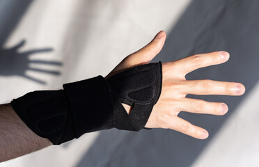 A close-up of a man's right hand, which has a medical orthosis on the wrist joint for fixation. A...
