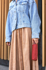 Stylish woman wearing denim jacket and flowing skirt with red umbrella accessory, modern fashion...