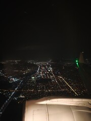 Nighttime urban landscape viewed from an airplane above a bustling city filled with lights and traffic along the highways