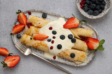 Crepes, blinis or thin pancakes with strawberries, whipped cream and blueberries on a plate on...