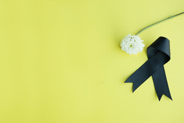 Black funeral ribbon and white flower on yellow background. Space for text