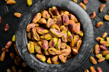 Stone mortar with pistachio kernels, preparation of pistachio flour. Macro photo, close-up, on a black slate table.