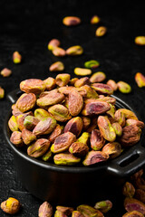 Pistachios. Black stone bowl with peeled roasted pistachio kernels. Close-up on a black stone background.