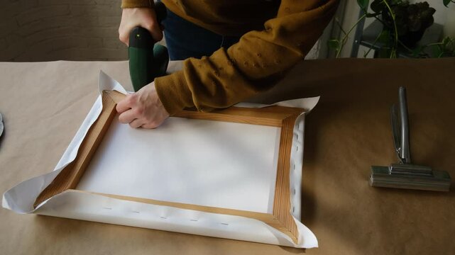 Process of stretching canvas onto stretcher bars using staple gun in workshop.