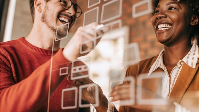 A pair of colleagues sharing a laugh as they interact with a holographic brainstorming session sticky notes and ideas floating around them creating a collaborative learning