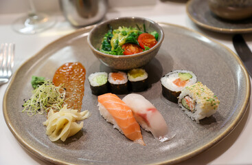 Ein Teller mit Salat und Sushi Rollen, frischer roher Fisch.
