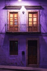 Obraz premium Old purple building facade with a balcony and windows at night in the city of Guanajuato, Mexico, illuminated by warm street light