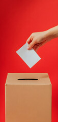 Obraz premium Hand inserting empty paper into gray ballot box. Hand placing vote into ballot box isolated on red background. Election, civic engagement or citizen voting concept. Banner with copy space.