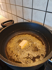 top view of a cooking pot on a gas stove with melted butter, margarine. The butter is partially melted. A lump of butter is still in the pot.