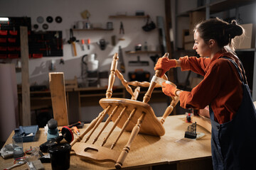 woman repairing wooden chair in workshop