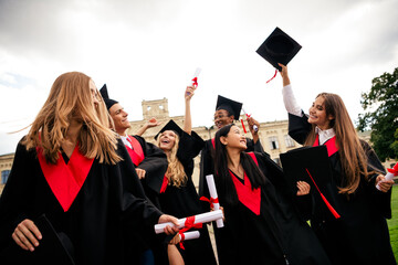 Joyful graduates celebrate on a sunny campus day, tossing mortarboards and holding diplomas in...