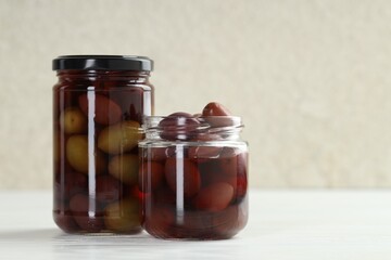 Pickled olives in glass jars on white wooden table, closeup. Space for text