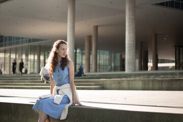 Girl sitting on steps in denim dress and sneakers. Student, studies, prospects, youth. Sunny weather. Admission.