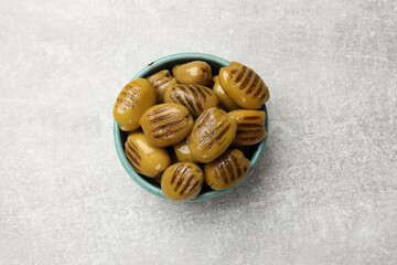 Grilled green olives in bowl on gray textured table, top view