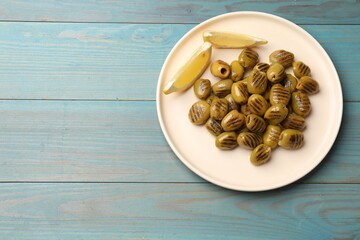 Grilled green olives and lemon wedges on light blue wooden table, top view. Space for text